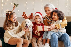 A family in Christmas attire gathered on a couch and opening a gift.