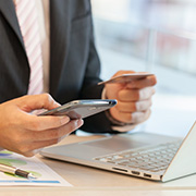 A man using his phone while sitting at his laptop going over finances.