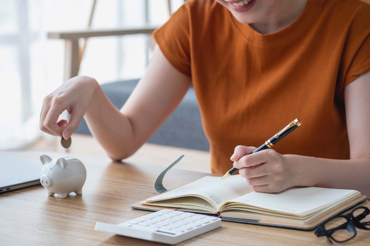 A young woman putting a coin into a small piggy bank.