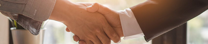 A person shaking hands with a banker over a table near a window with sunlight coming in