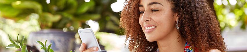 A woman smiling while using her credit card and phone at an outdoor café