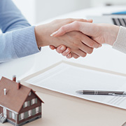 A customer shaking hands with their realtor next to a small model home on a desk.